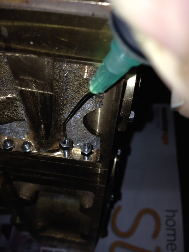 The needle tip is pushed into the end of the stud/bolt.  The nut slips onto the end of the stud, and is then spun with a finger tip until it engages with the thread.